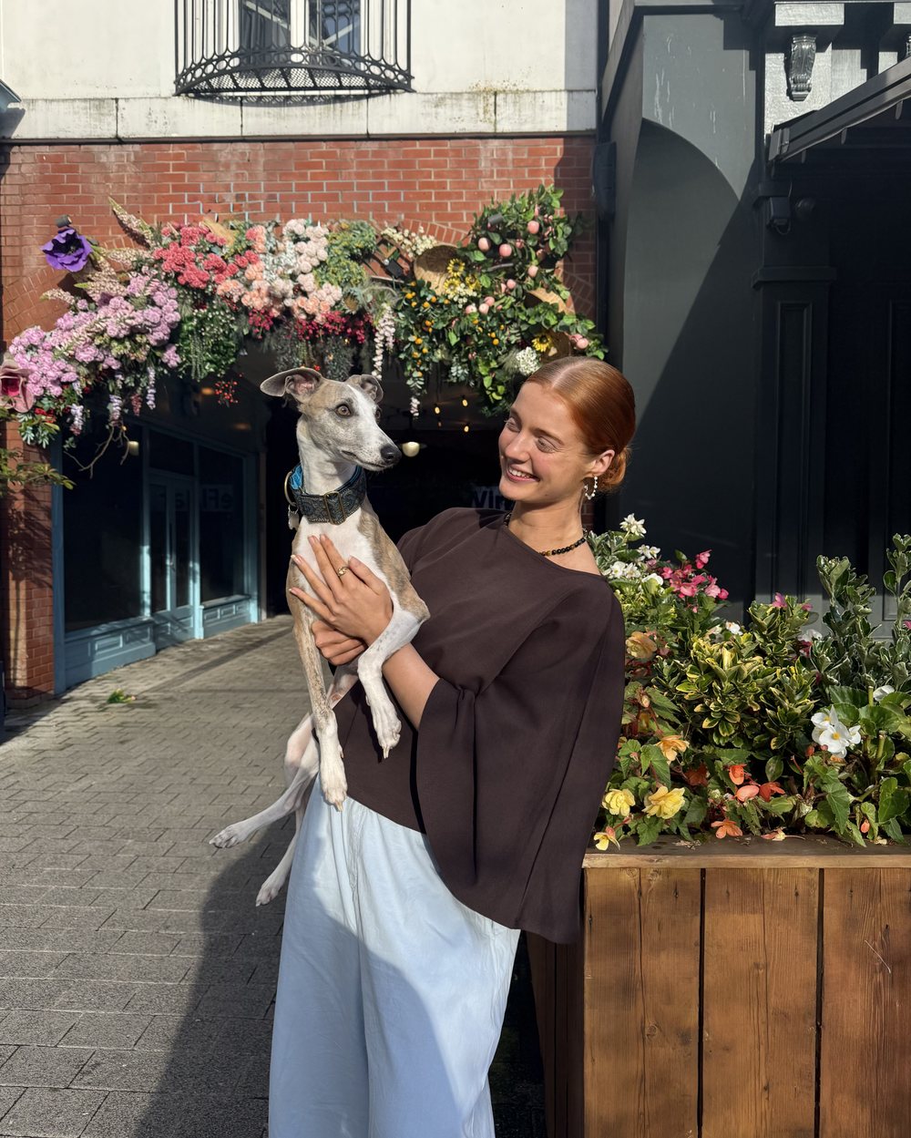 Bethy holding Blue the whippet in front of a flower-filled shopfront
